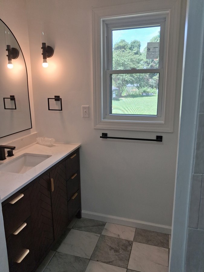 Bathroom with a dark wood vanity, light countertop, wall lights and white window trim