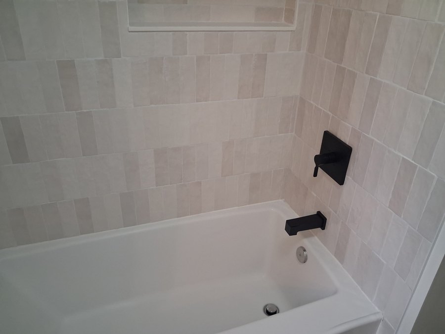 White bathtub with a light tile surround and black fixtures